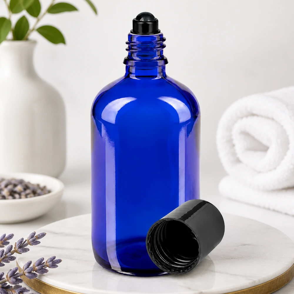 Flacone roll-on 100ml blu STD nero ApoGlas Flacone di vetro blu da 100 ml con sfera rotante nera e tappo rimosso, appoggiato su una base di marmo