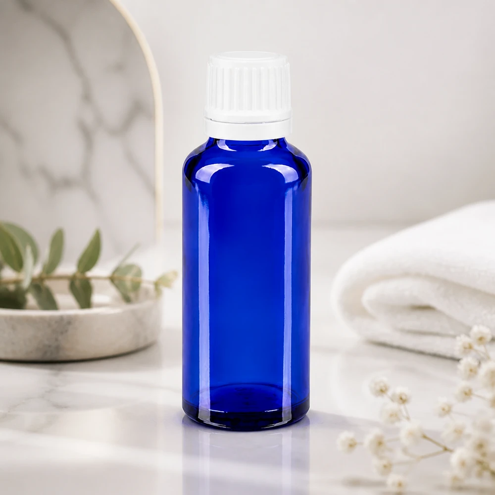 Flacone contagocce blu da 30ml OV bianco/0,7mm ApoGlas Flacone da farmacia blu da 30 ml con dosatore a gocce da 0,7 mm su marmo bianco accanto a un asciugamano piegato