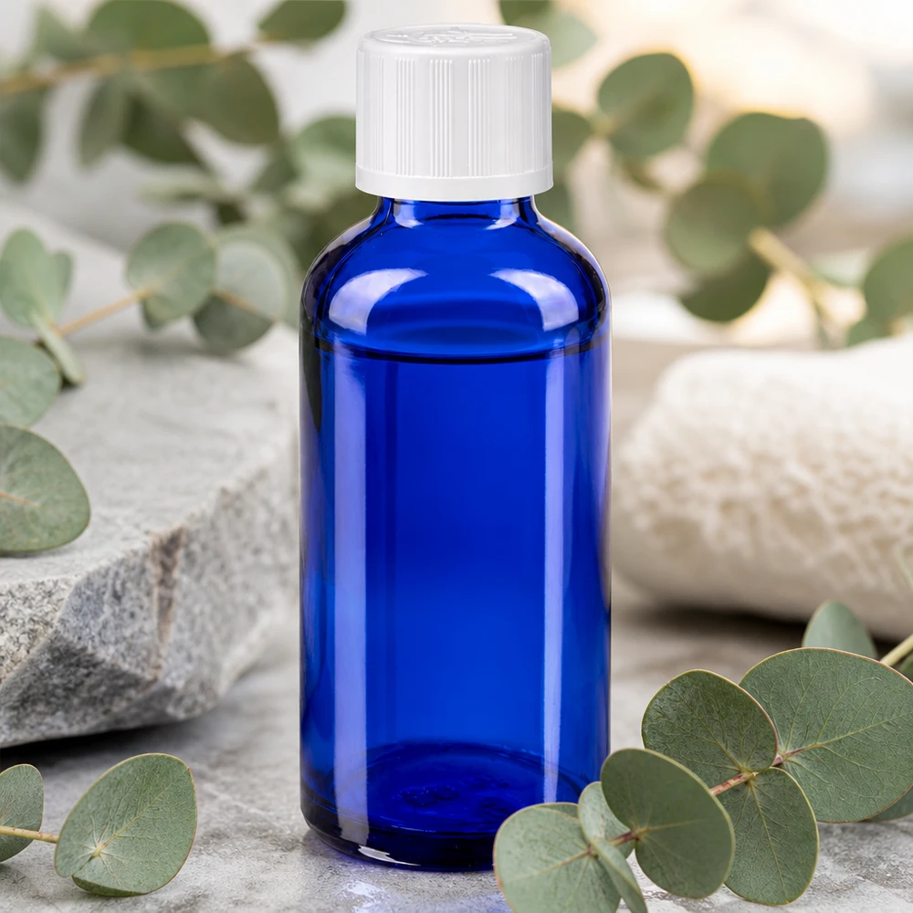 Flacone da farmacia da 50 ml blu cobalto con tappo KiSi bianco, appoggiato su una pietra naturale tra rami di eucalipto