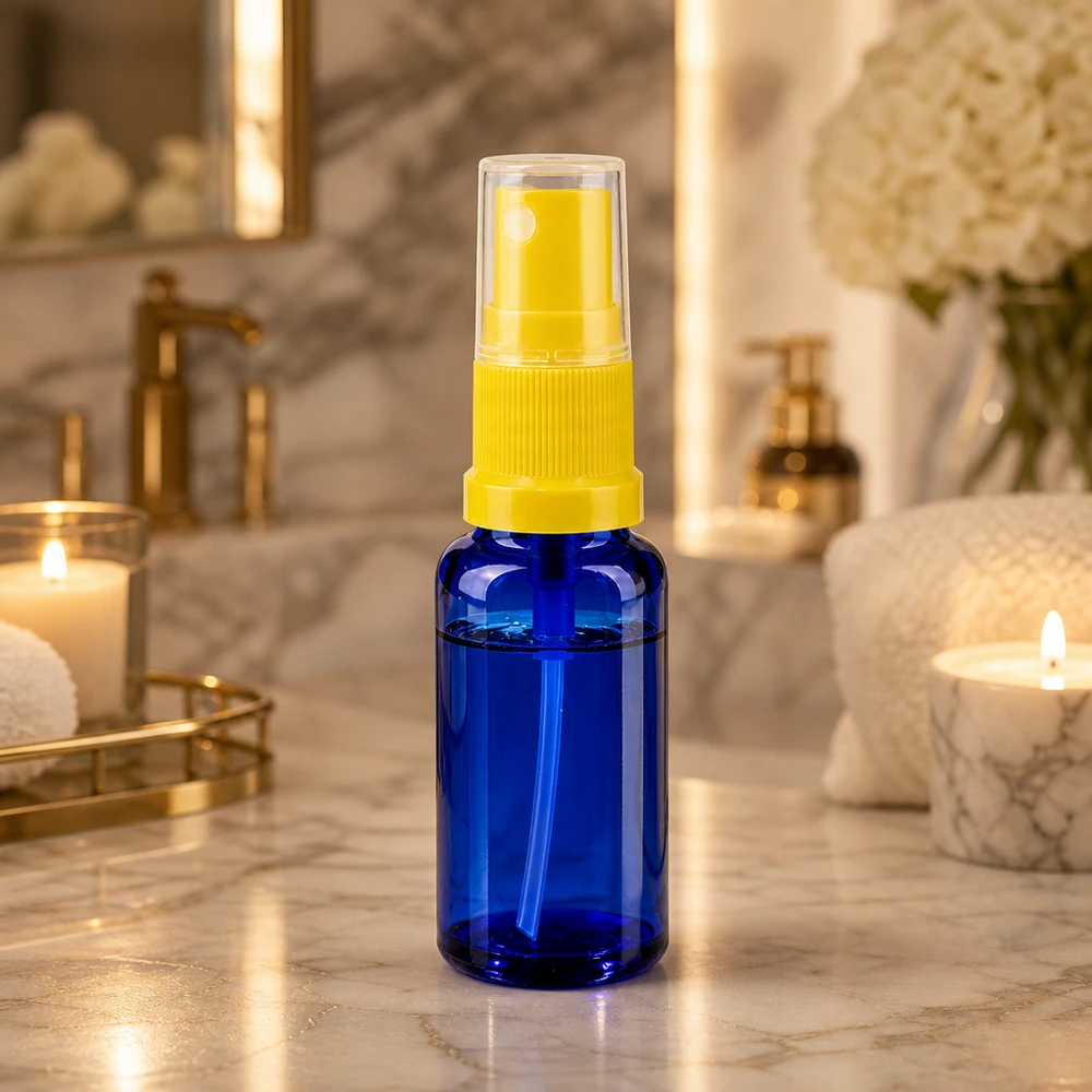 Flacone spray in vetro blu da 20 ml con erogatore giallo su un ripiano da bagno in marmo