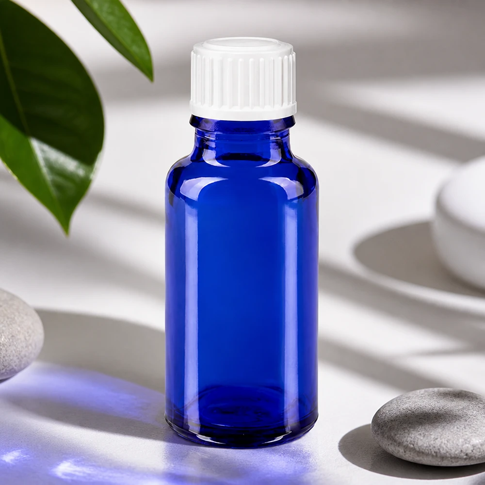 Flacone di vetro blu da 20 ml con tappo bianco accanto a pietre naturali e foglie verdi