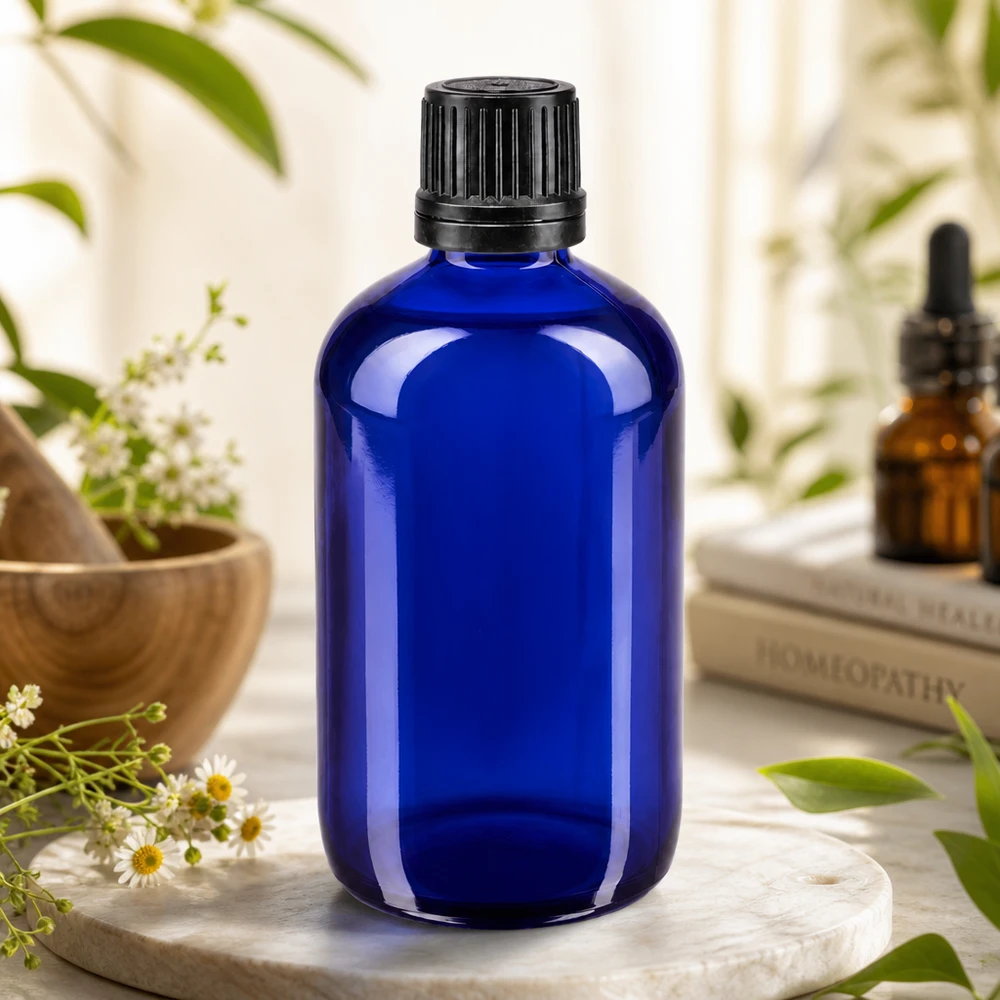 Flacone di vetro da farmacia blu da 100 ml con tappo nero a coste, tra fiori di camomilla ed erbe medicinali