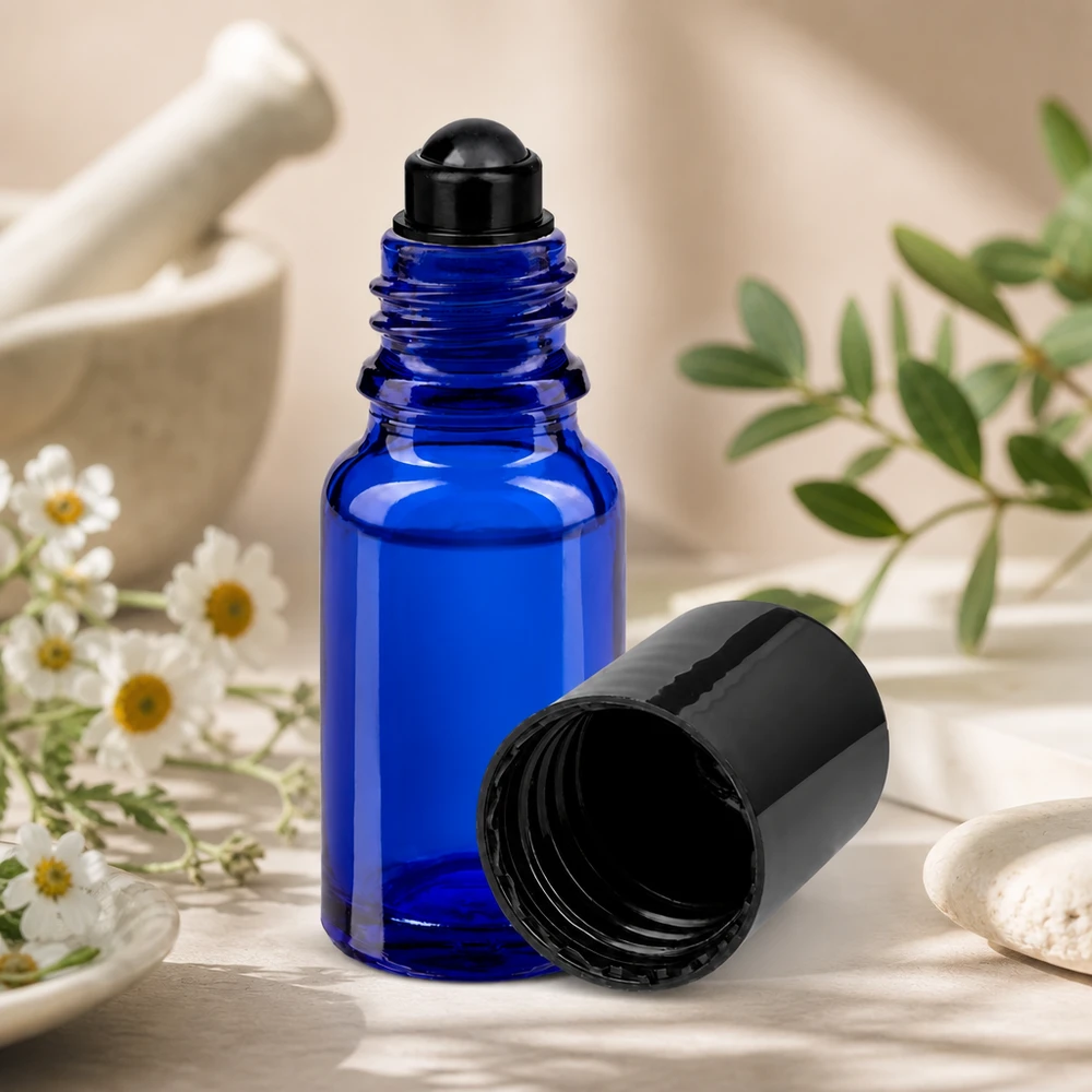 Flacone roll-on 10ml blu STD nero ApoGlas Flacone roll-on blu da 10 ml STD con tappo nero accanto a erbe da mortaio e fiori di camomilla