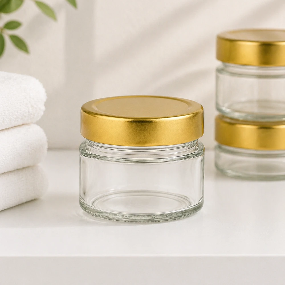 Barattolo rotondo da 80 ml con coperchio BasicSeal oro profondo UNiTWIST. Barattolo rotondo da 80 ml con coperchio BasicSeal oro intenso in un ambiente bagno con asciugamani bianchi per cosmetici