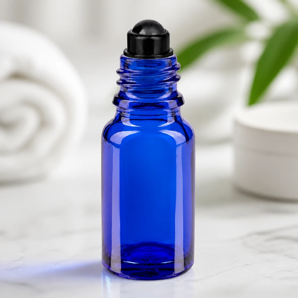 Flacone roll-on 10ml blu STD nero ApoGlas Flacone di vetro blu da 10 ml con applicatore roll-on nero su marmo, su sfondo bianco