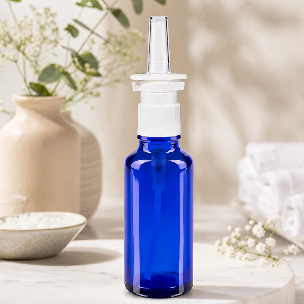 Primo piano di un flacone spray nasale da 30 ml, blu cobalto, con erogatore a vite bianco e puntale in plastica trasparente