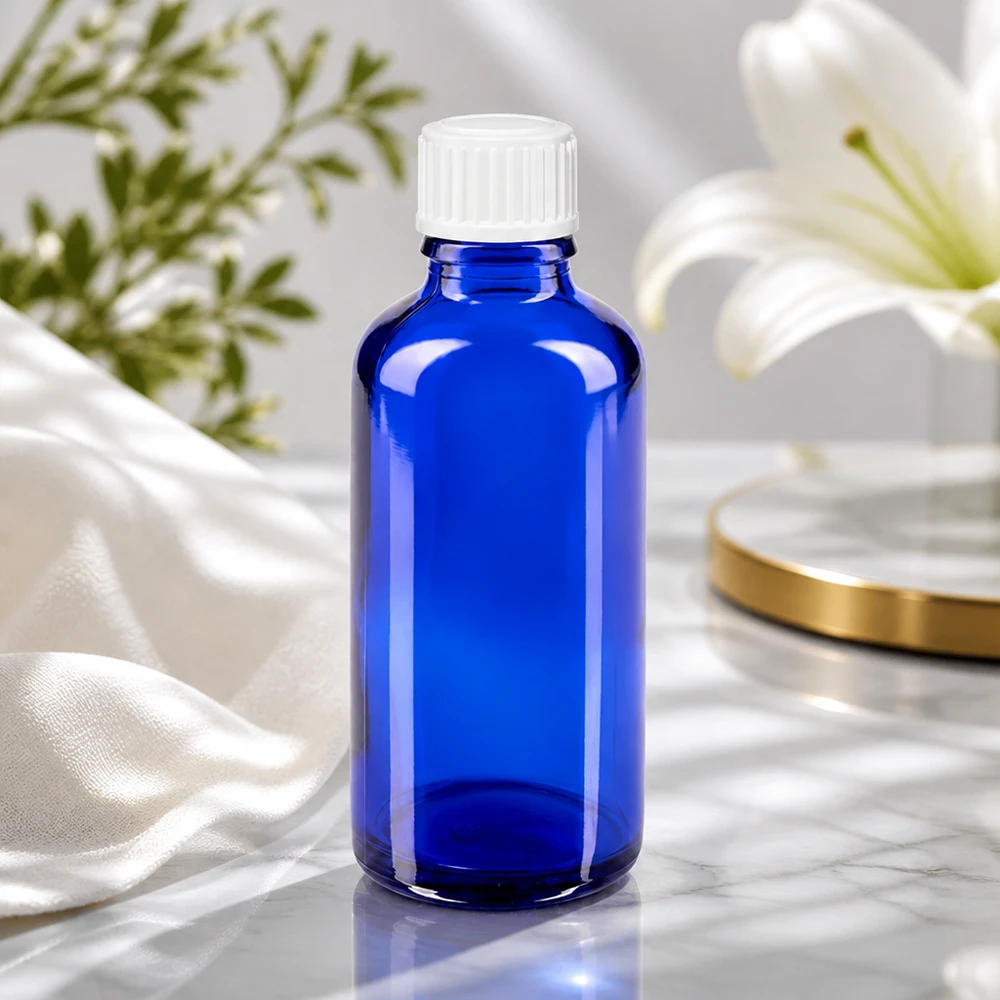 Flacone di vetro blu da 50 ml con tappo a vite bianco accanto a un giglio bianco su una superficie di marmo