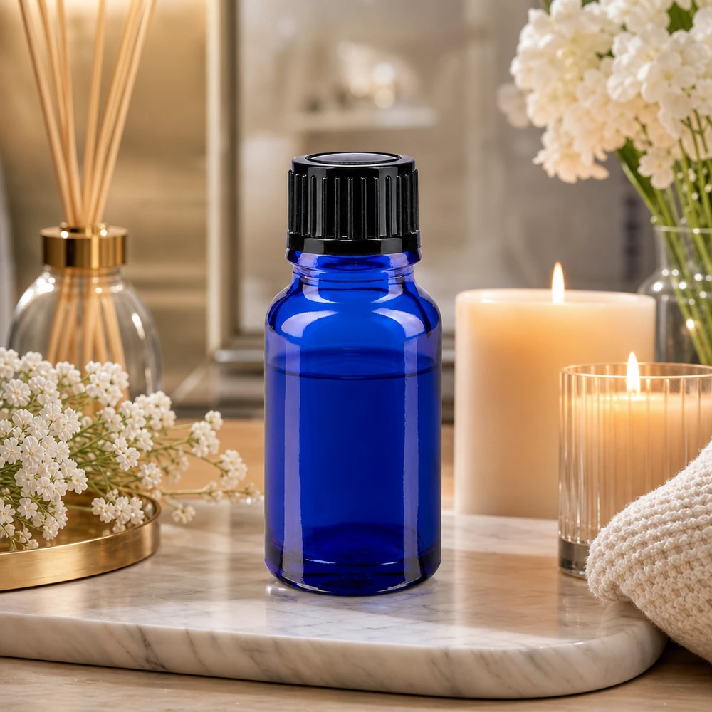 Piccola boccetta di vetro blu da 10 ml con tappo nero su un vassoio di marmo accanto a delle candele