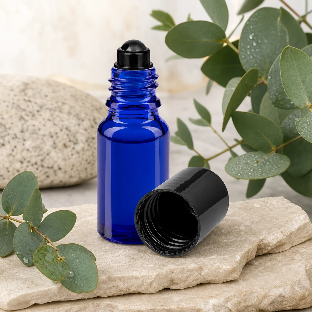 Flacone roll-on 10ml blu STD nero ApoGlas Flacone roll-on ApoGlas blu da 10 ml con tappo nero, accanto a ramoscelli di eucalipto su una pietra naturale