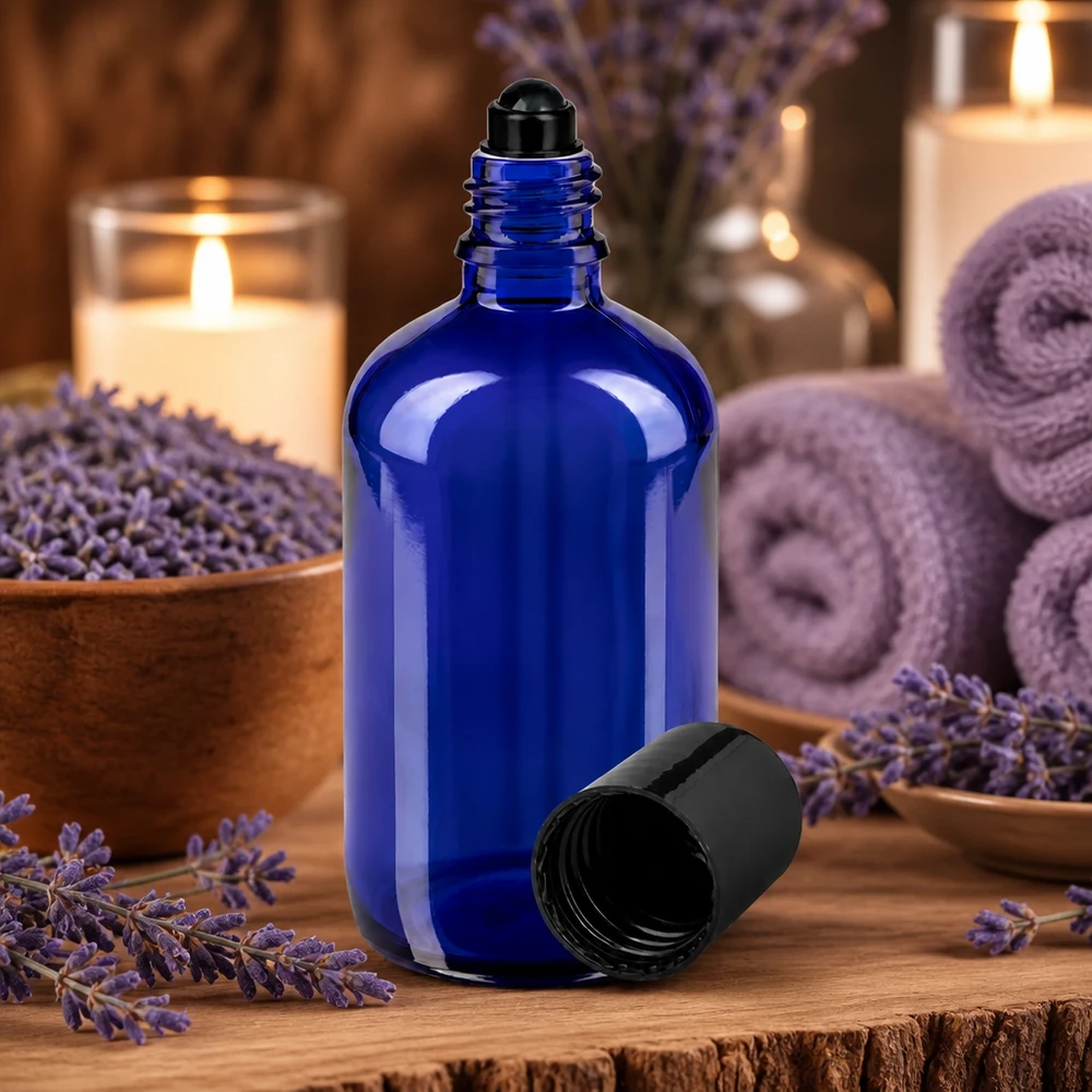 Flacone roll-on 100ml blu STD nero ApoGlas Flacone di vetro blu da 100 ml con tappo roll-on, circondato da fiori di lavanda e candele