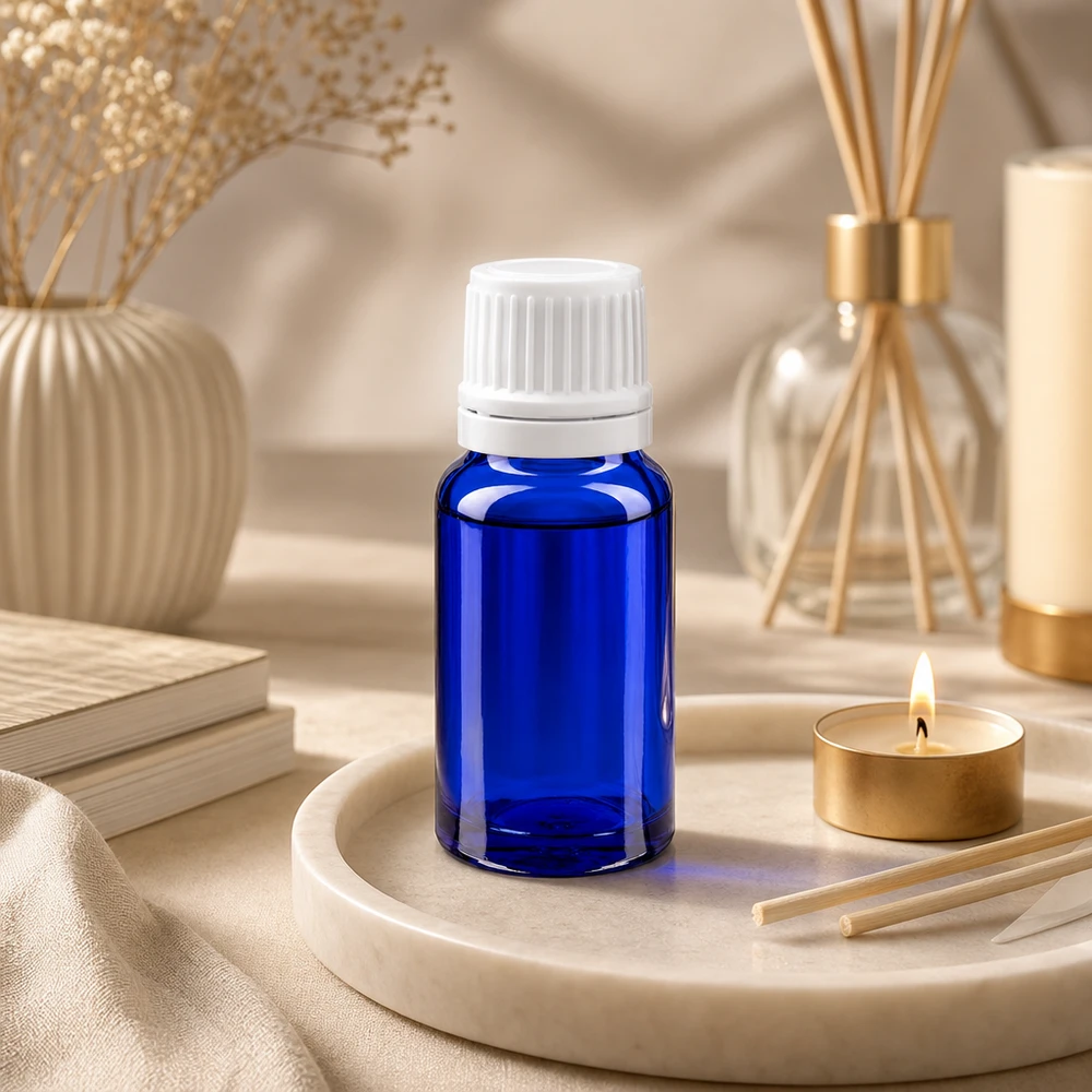 Flacone contagocce blu da 10ml OV bianco/0,7mm ApoGlas Piccola bottiglietta di vetro blu con tappo a vite bianco su un vassoio di marmo accanto a una candela da tè