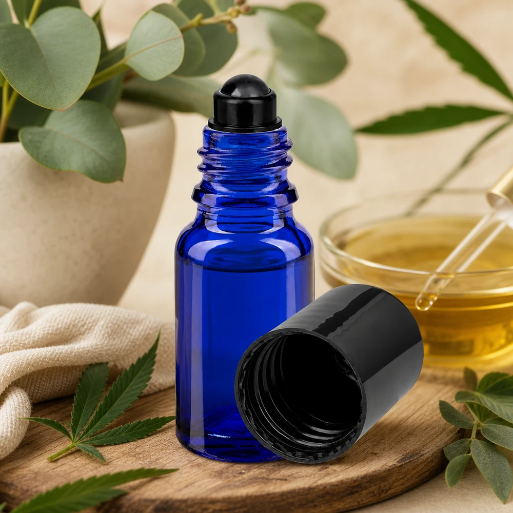 Flacone roll-on 10ml blu STD nero ApoGlas Flacone roll-on ApoGlas blu da 10 ml con tappo nero su un tagliere di legno, accanto a una foglia di cannabis e a un ramoscello di eucalipto