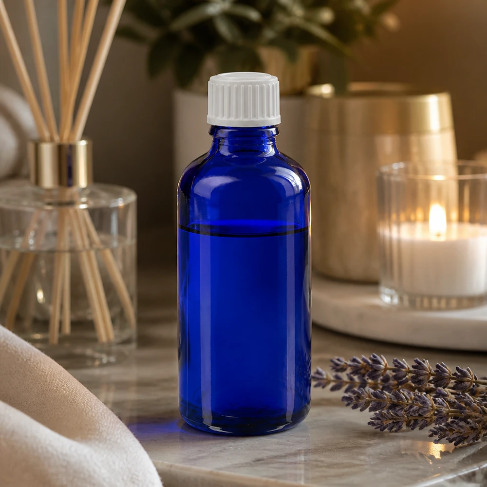 Flacone in vetro blu da 50 ml con tappo contagocce su una base di marmo, accanto a un mazzetto di lavanda e a un diffusore di profumo per ambienti