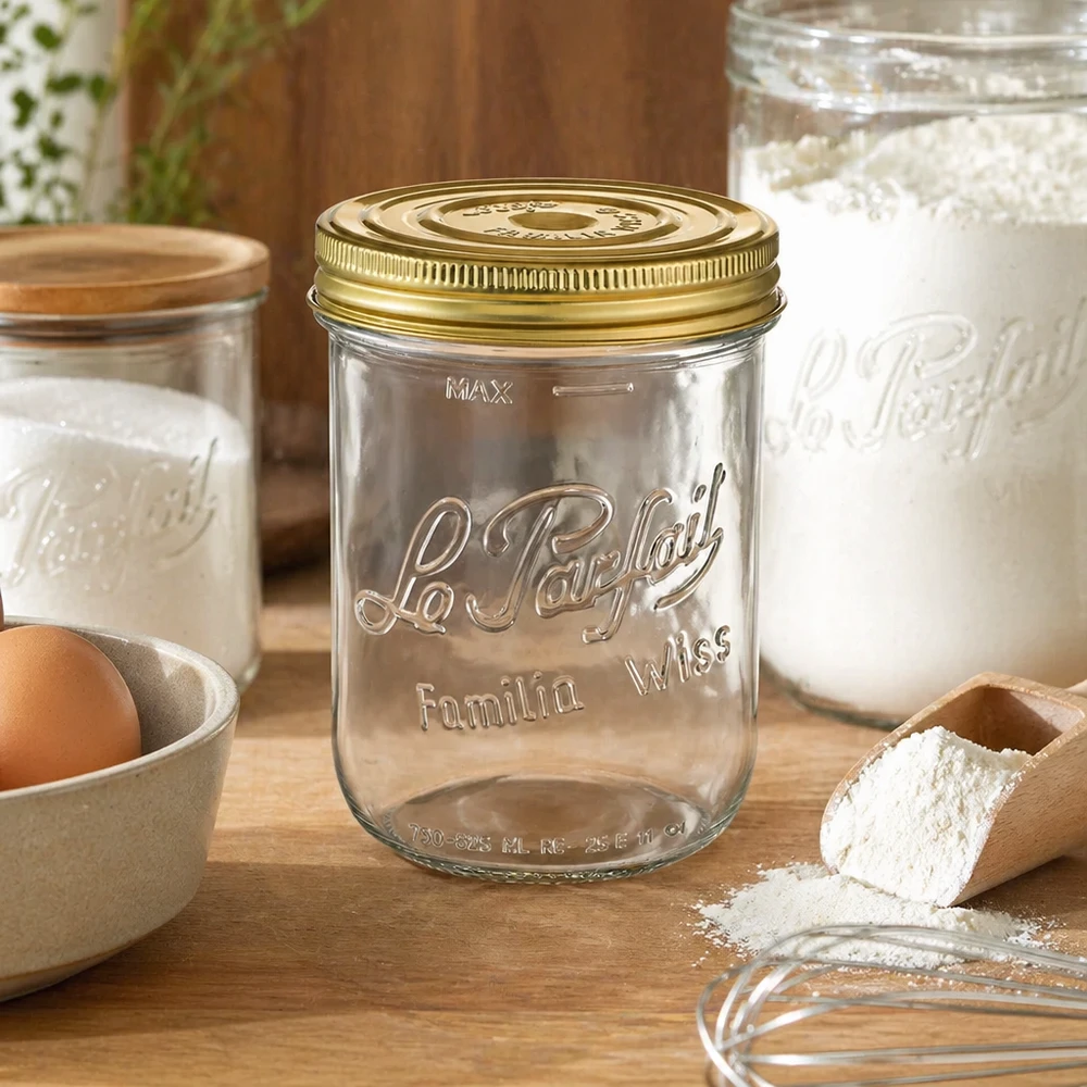Vasetto Familia Wiss da 1020 ml con coperchio dorato sul tavolo di legno accanto a ingredienti da forno e altri vasetti per conserve