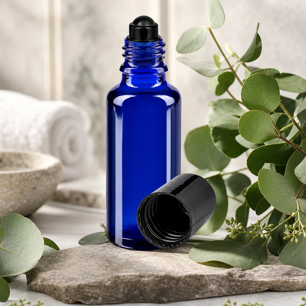 Flacone roll-on 30ml blu STD nero ApoGlas Flacone di vetro da 30 ml blu cobalto con applicatore roll-on nero su una pietra naturale tra rami di eucalipto