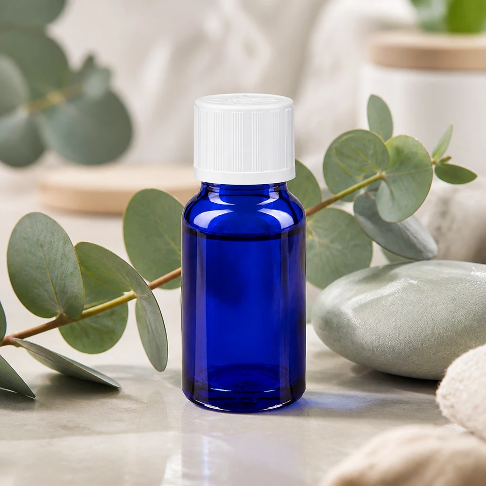 Flacone da farmacia da 10 ml blu cobalto con tappo bianco KiSi, davanti a rami di eucalipto su marmo