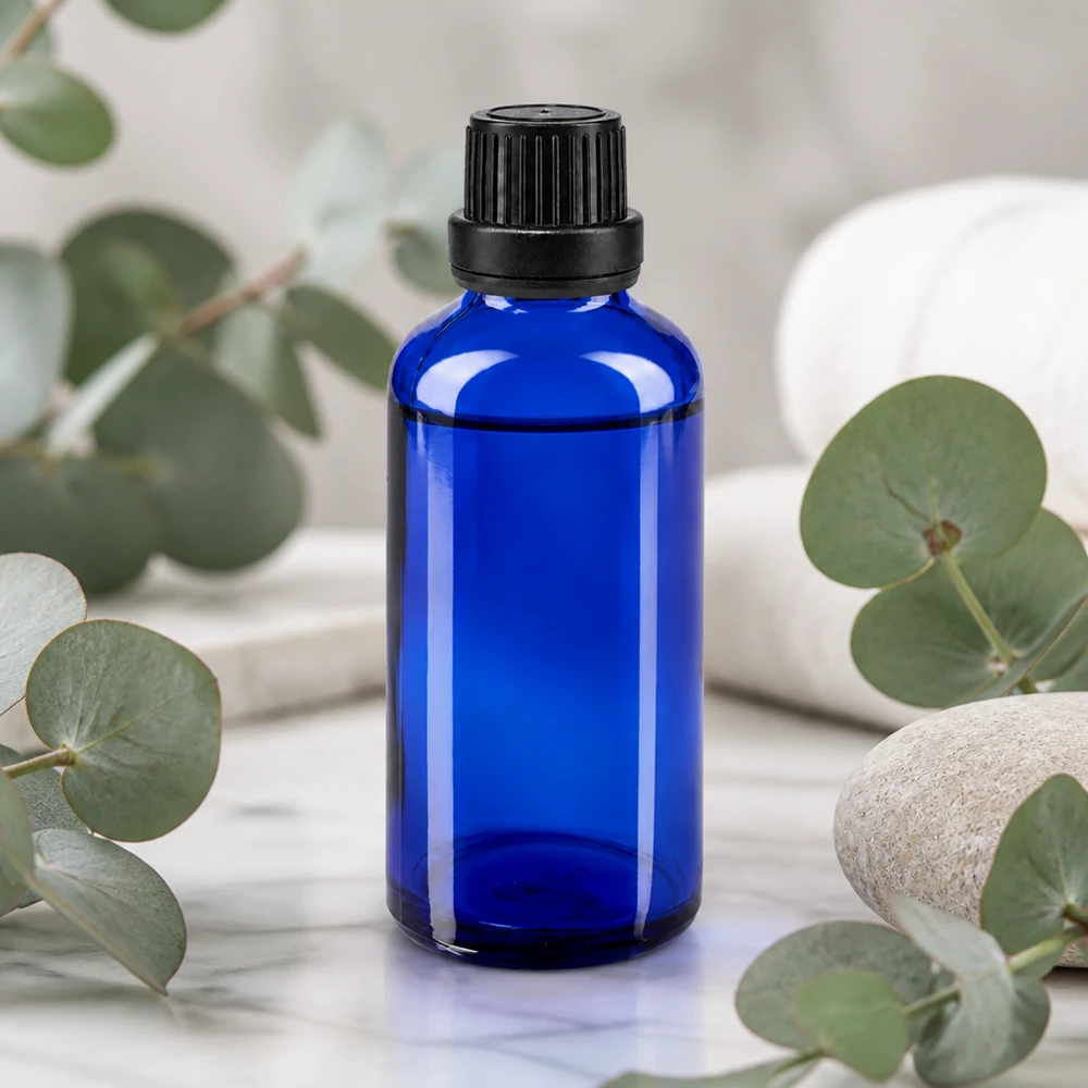 Fiaschetta da farmacia da 50 ml di colore blu cobalto con tappo di sicurezza nero a prova di bambino, davanti a rami di eucalipto