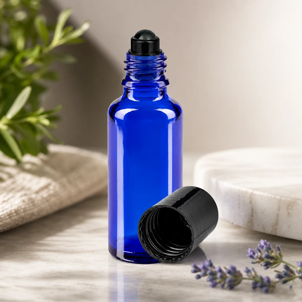 Flacone roll-on 30ml blu STD nero ApoGlas Flacone di vetro roll-on da 30 ml color blu cobalto con tappo nero, accanto a un rametto di lavanda e uno di rosmarino