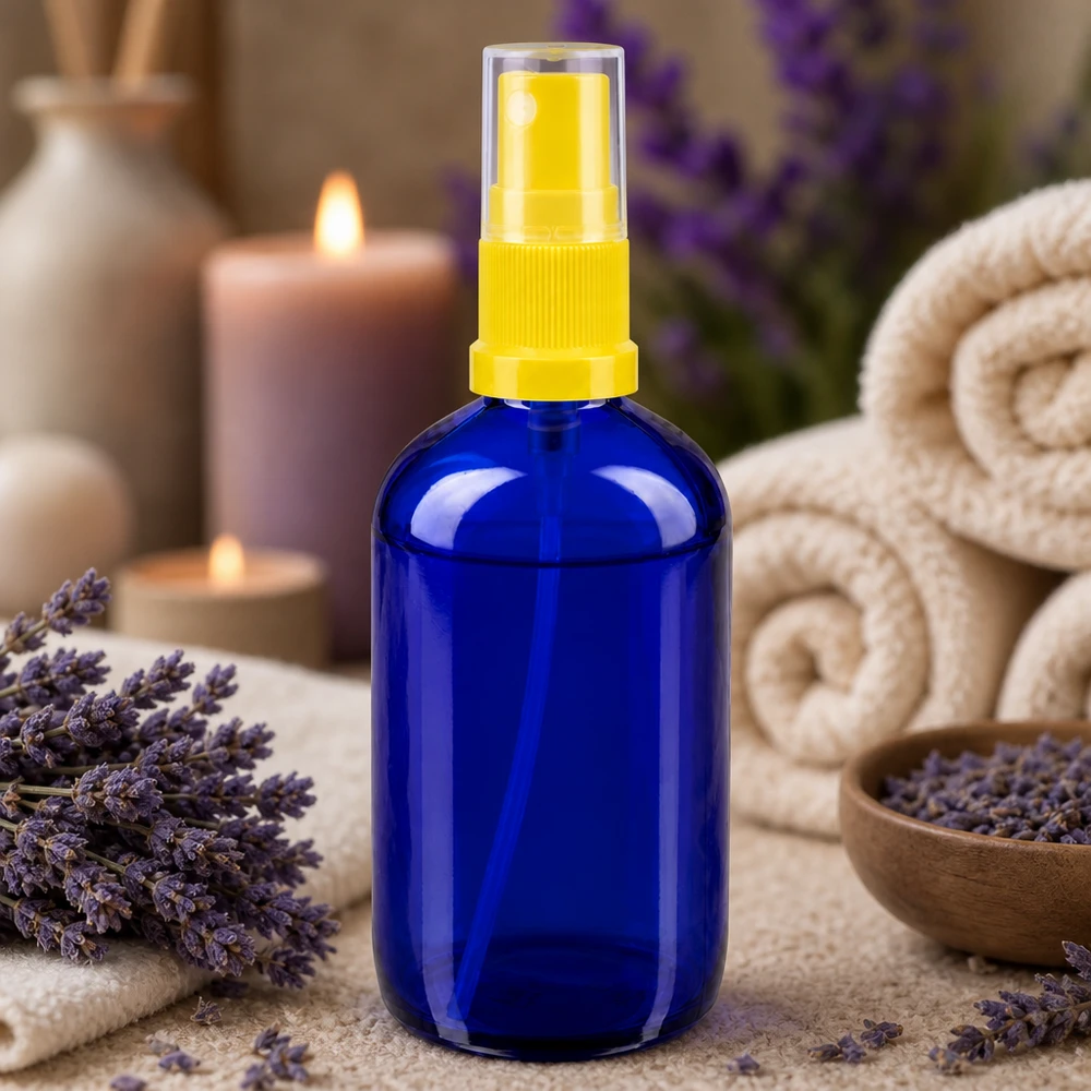 Piccola bottiglietta di vetro blu da 100 ml con erogatore a spruzzo giallo, circondata da lavanda e candele