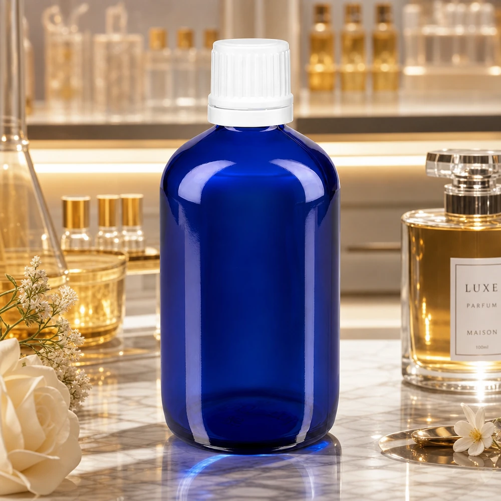Bottiglia da farmacia blu da 100ml. SV OV bianco/11mm ApoGlas Flacone da farmacia in vetro blu da 100 ml con tappo OV bianco da 11 mm su un piano in marmo accanto a un profumo di lusso