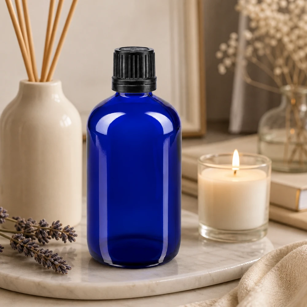 Flacone di vetro blu da 100 ml con tappo contagocce nero, su un vassoio di marmo con lavanda e una candela