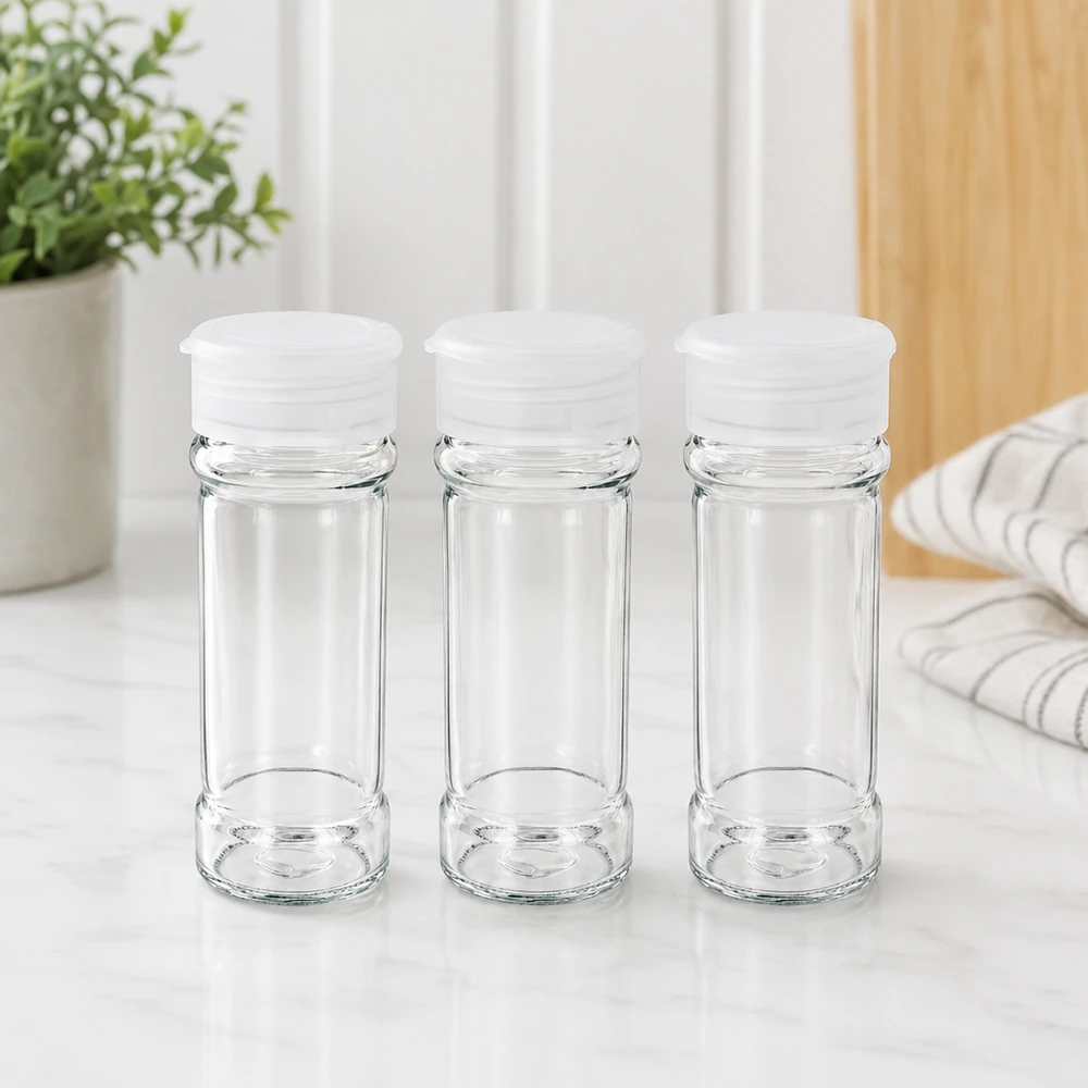 Tre barattoli per spezie in vetro trasparente da 100 ml con coperchi dosatori bianchi su una superficie in marmo