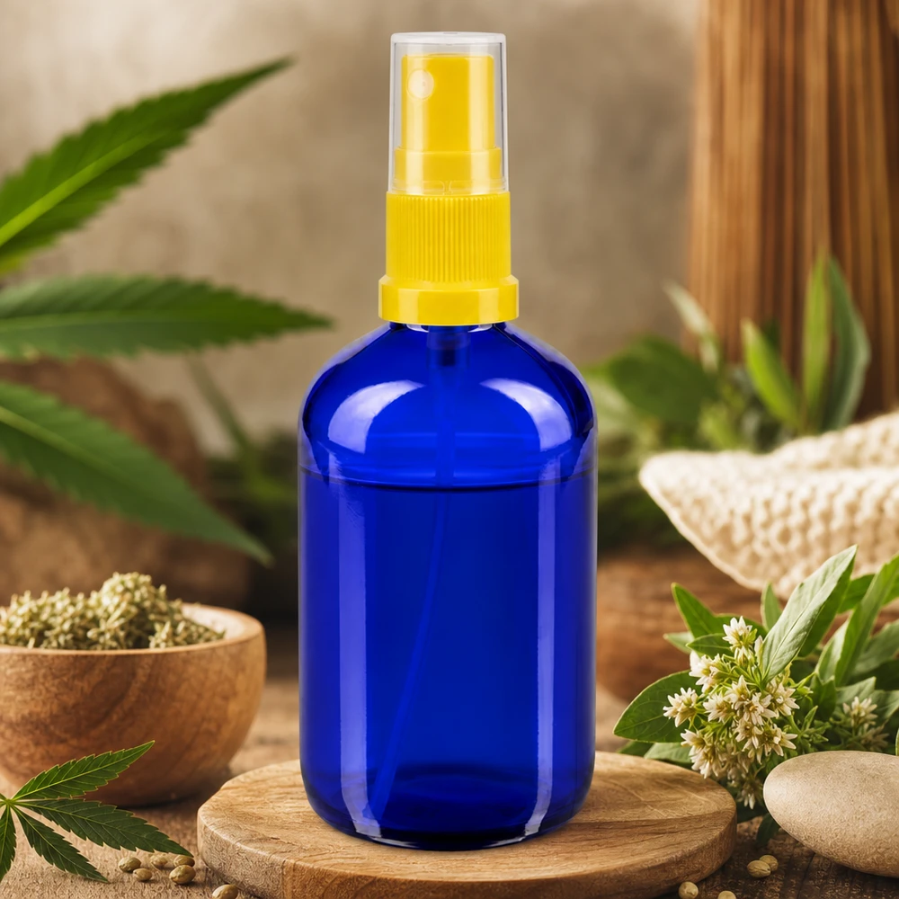 Flacone di vetro blu da 100 ml con erogatore a spruzzo giallo, circondato da piante di canapa ed erbe naturali