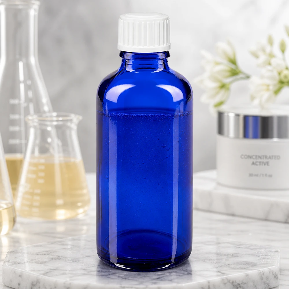 Flacone di vetro da 50 ml blu cobalto con tappo a vite bianco accanto a un matraccio da laboratorio e a una crema per la cura della pelle