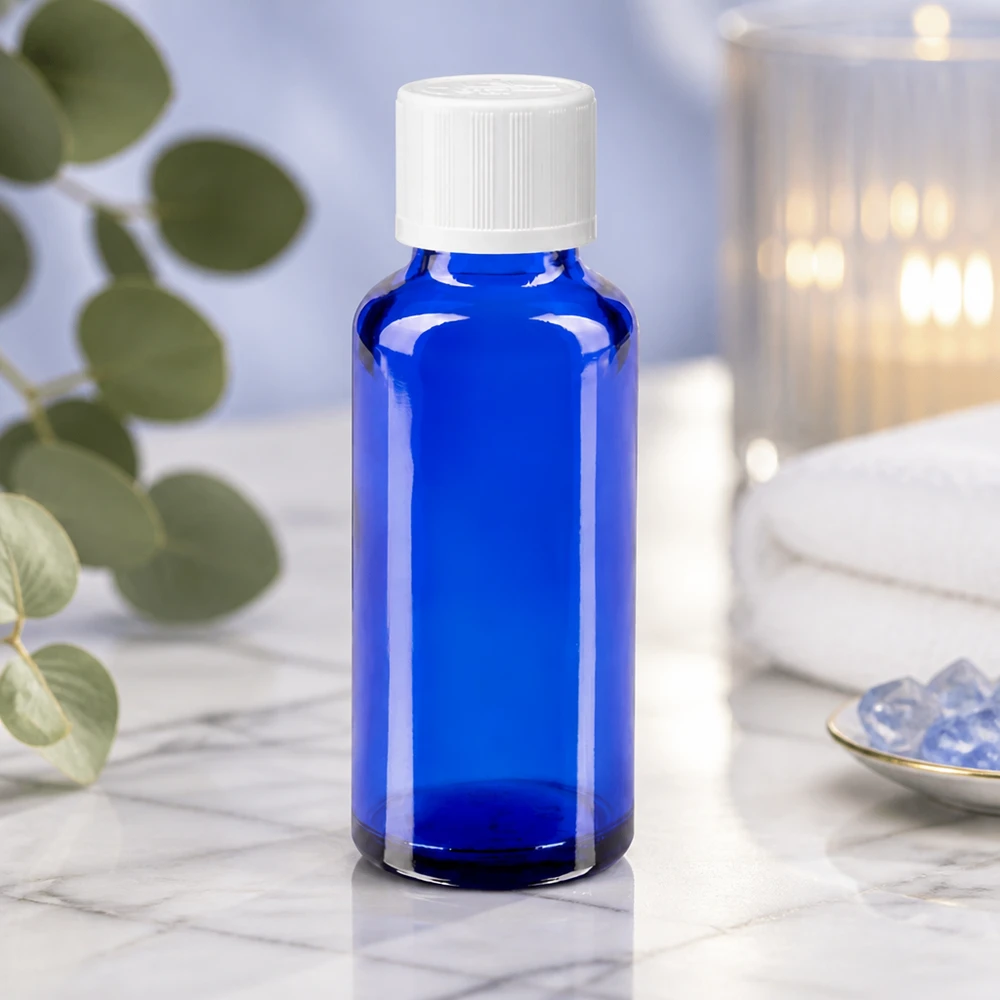 Vaso da farmacia blu da 30 ml con tappo a vite bianco su un piano di marmo bianco, accanto a cristalli e una candela