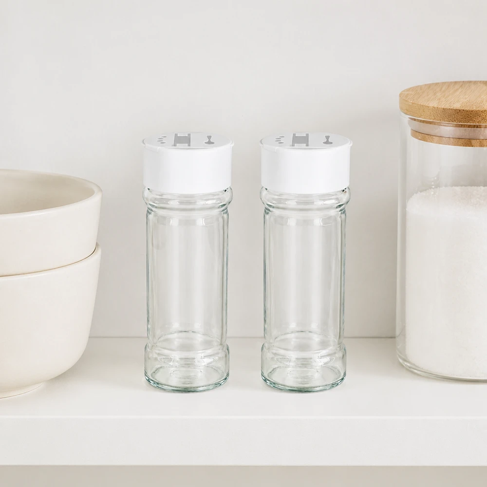 Barattolo per sale/spezie da 100 ml con doppio dosatore, bianco Due barattoli per spezie da 100 ml con coperchio bianco a doppia spargitrice, affiancati su uno scaffale bianco