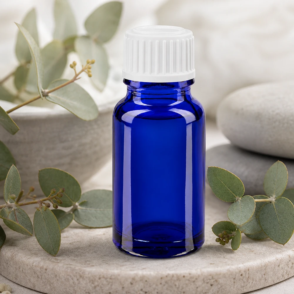 Flacone di vetro da 10 ml blu cobalto con tappo standard bianco tra rami di eucalipto