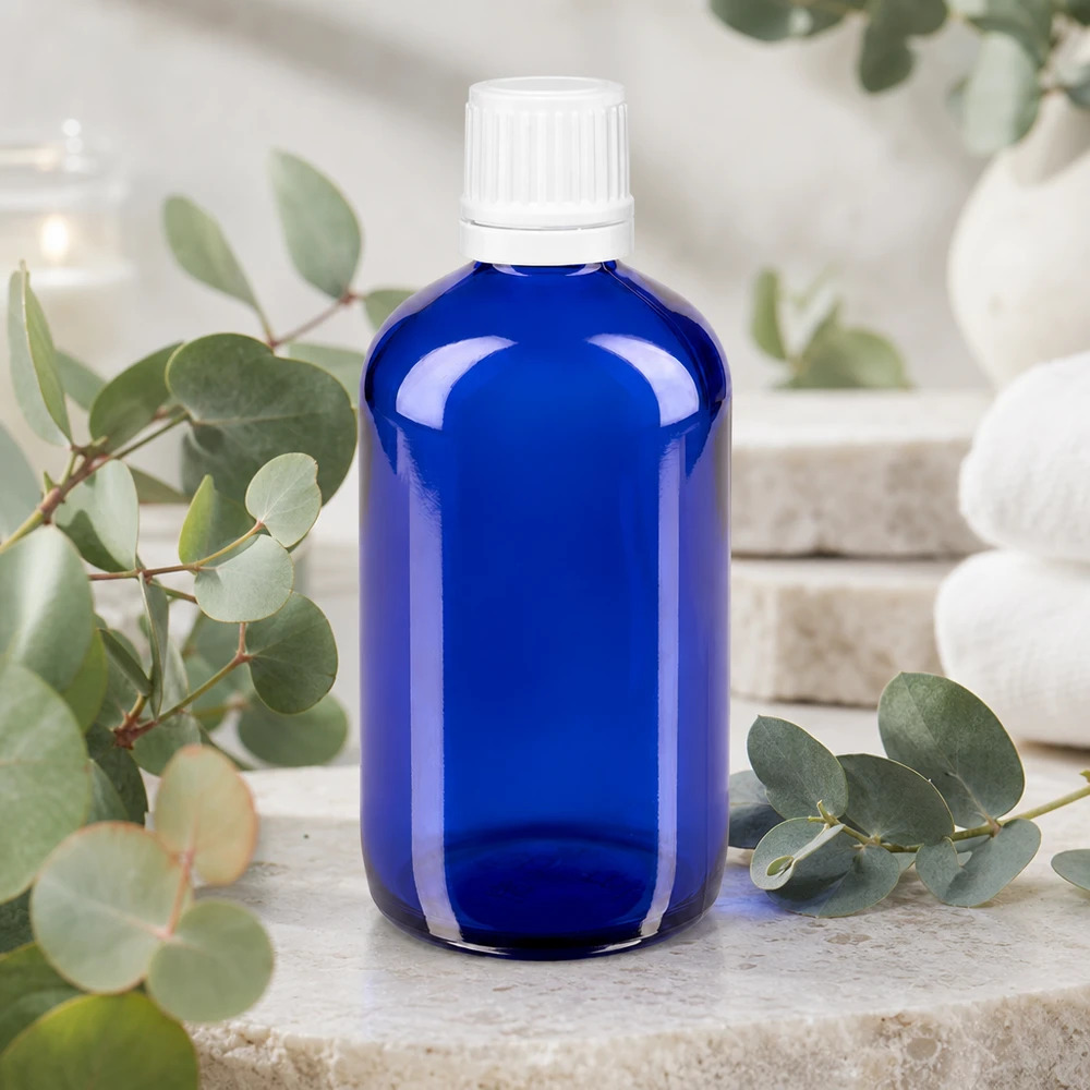 Flacone da farmacia blu cobalto da 100 ml con tappo di sicurezza bianco, appoggiato su una pietra naturale con ramoscelli di eucalipto