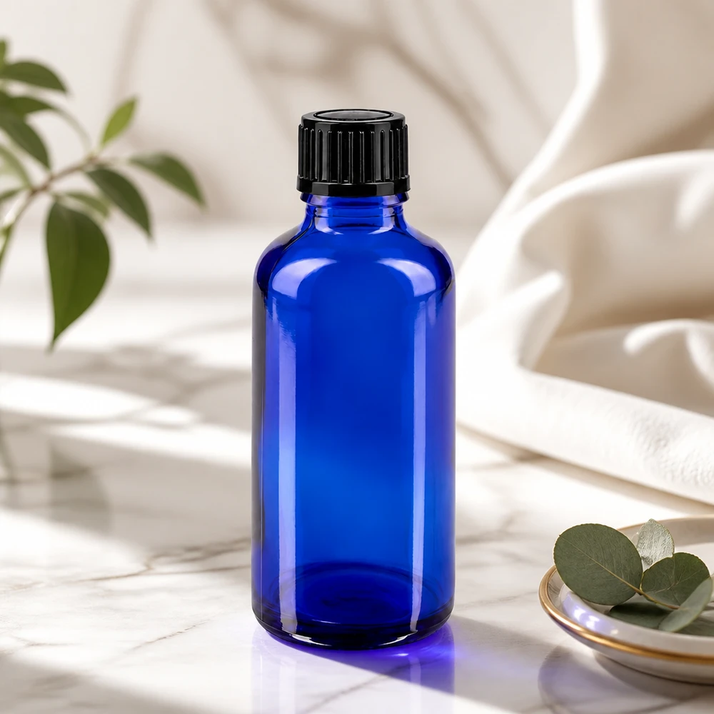 Bottiglia da farmacia blu da 50ml. SV STD nero/11mm ApoGlas Bottiglia di vetro blu da 50 ml con tappo nero su una superficie di marmo accanto a foglie di eucalipto