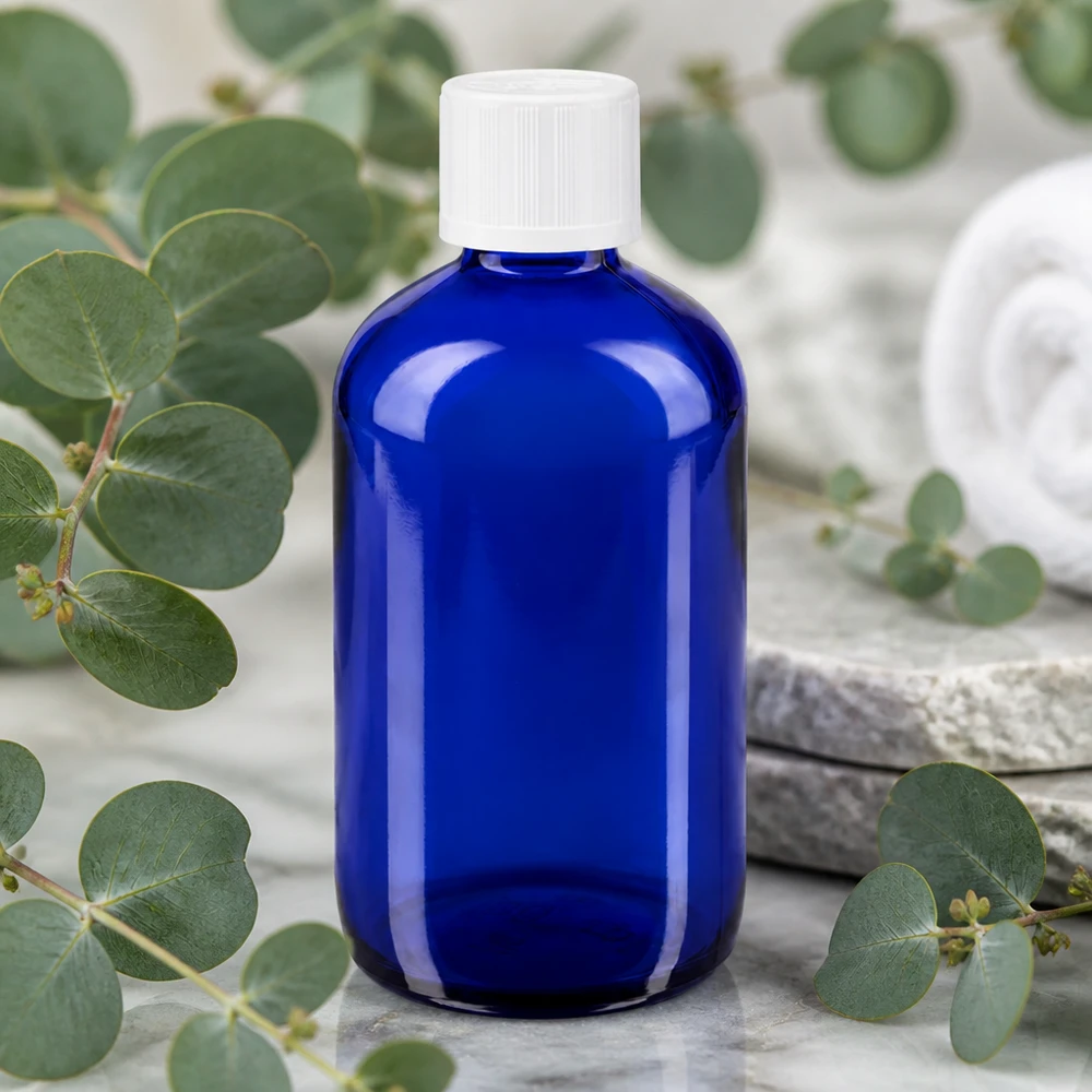 Flacone contagocce blu da 100 ml in vetro da farmacia con tappo bianco KiSi tra rami di eucalipto