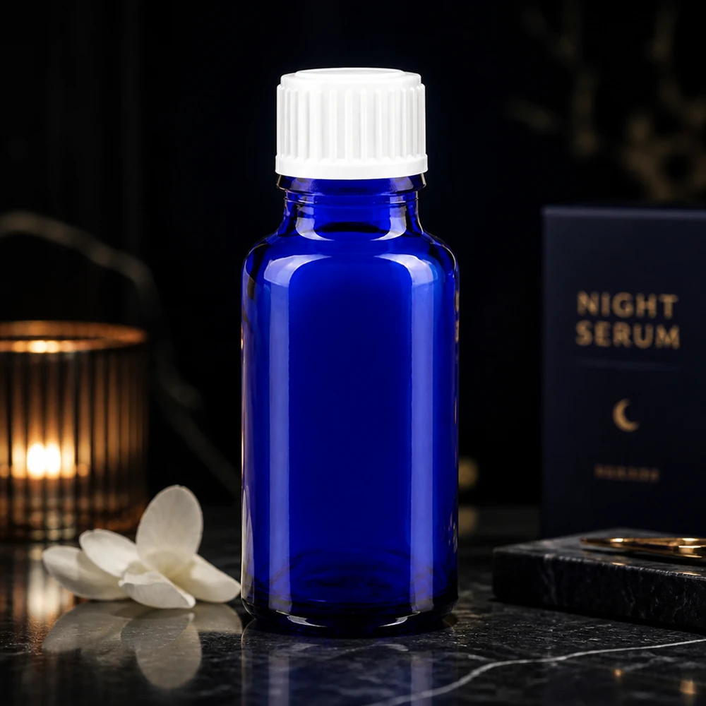 Flacone di vetro da 20 ml blu cobalto con tappo bianco accanto alla confezione del siero da notte su uno sfondo scuro