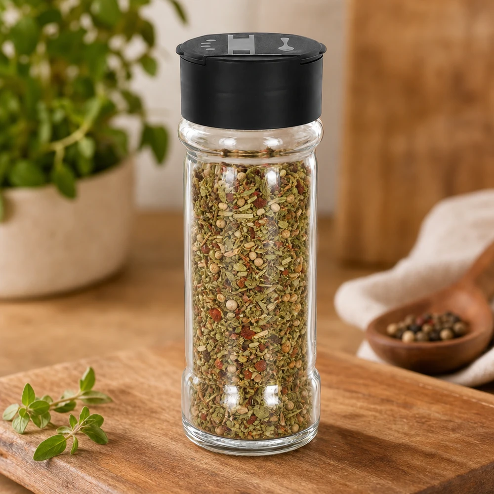 Miscela di erbe aromatiche in un contenitore per spezie in vetro trasparente da 100 ml con doppio coperchio nero, su un tagliere di legno