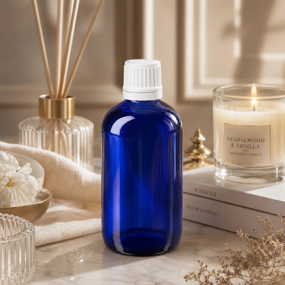 Flacone da farmacia blu in vetro da 100 ml con tappo bianco a prova di bambino, appoggiato su una base di marmo accanto a una candela al legno di sandalo