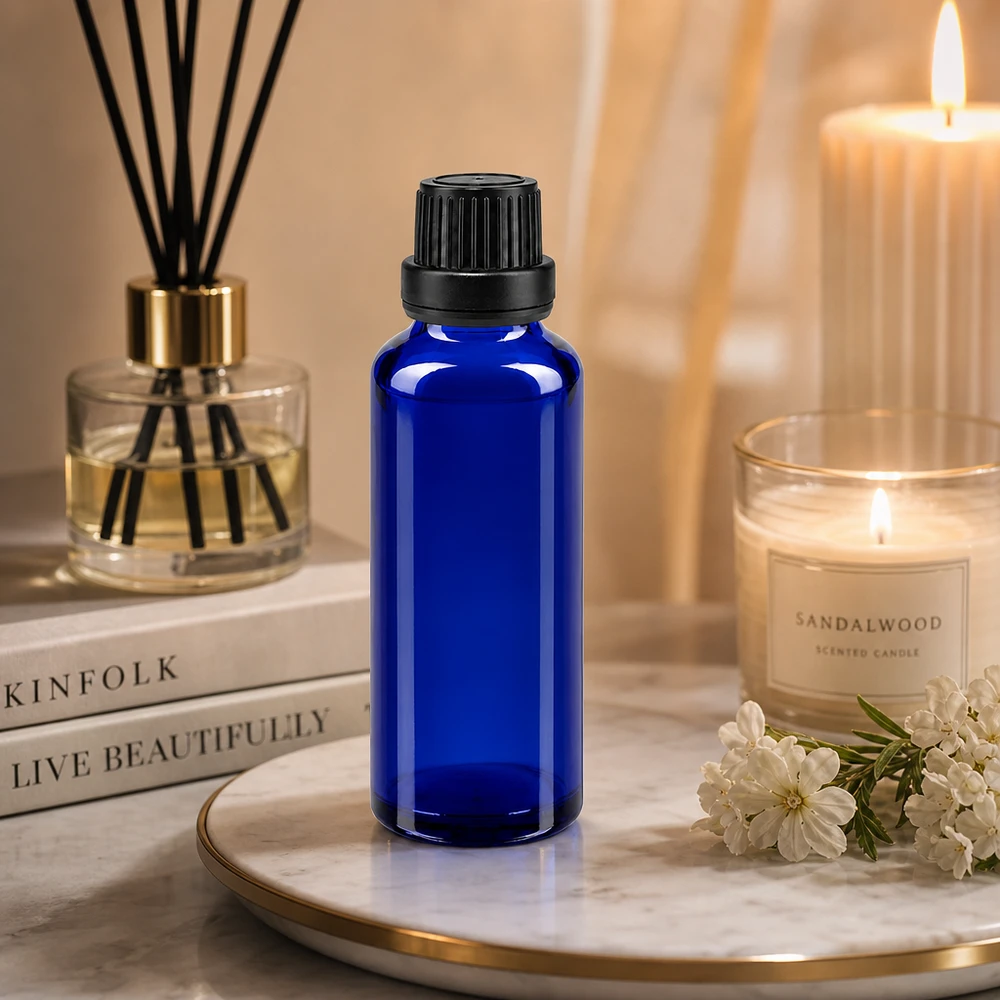 Flacone di vetro blu da 30 ml con tappo OV nero su un vassoio di marmo, accanto a una candela al legno di sandalo e a un diffusore