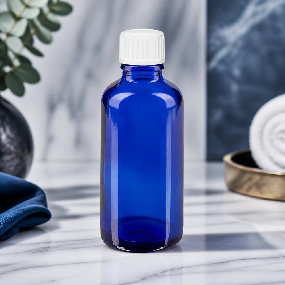 Flacone contagocce STD da 50 ml in vetro ApoGlas, colore blu cobalto, con tappo bianco su superficie marmorizzata