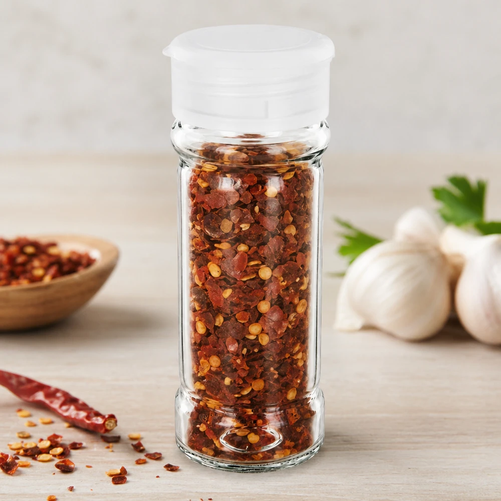 Barattolo per sale/spezie da 100 ml con dosatore, bianco Piccolo barattolo per spezie da 100 ml con dosatore bianco, riempito di fiocchi di peperoncino rosso e aglio sullo sfondo