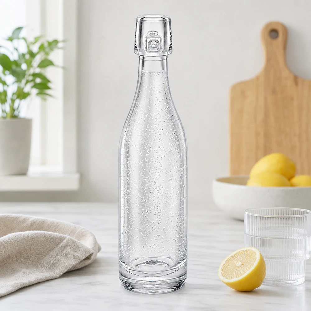 Bottiglia in vetro da 50 ml senza tappo UNiTWIST Bottiglia di vetro UNiTWIST da 50 ml riempita di acqua frizzante in una cucina moderna accanto a limoni e bicchieri piano di lavoro bianco