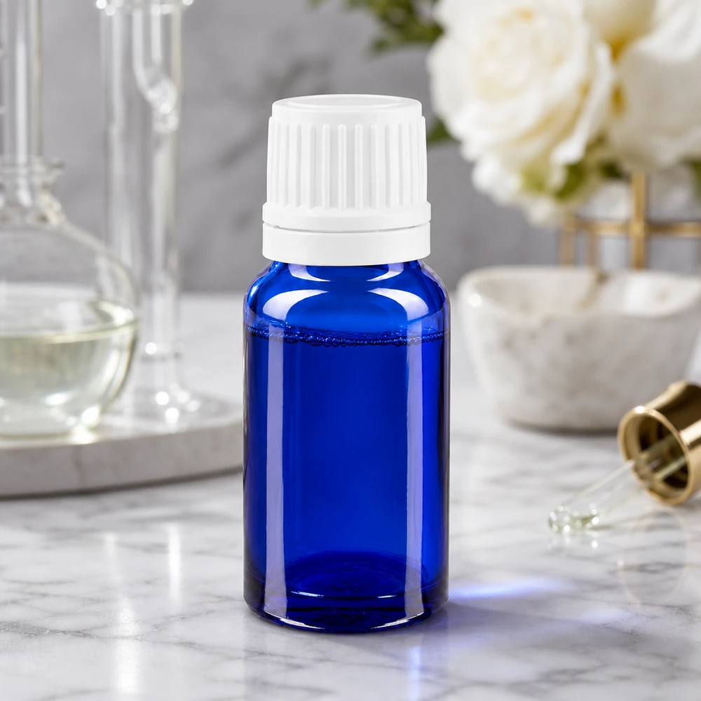 Flacone contagocce blu da 10ml OV bianco/0,7mm ApoGlas Flacone da farmacia da 10 ml in vetro blu con tappo contagocce bianco su una superficie di marmo accanto a delle rose