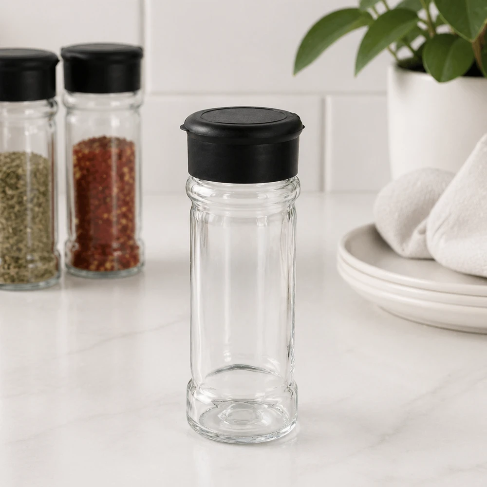 Piccola saliera in vetro da 100 ml con coperchio nero su un supporto in marmo bianco