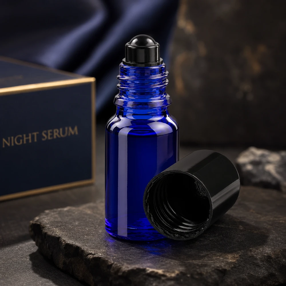 Flacone roll-on 10ml blu STD nero ApoGlas Flacone roll-on ApoGlas da 10 ml blu scuro con tappo nero aperto su una pietra di ardesia davanti alla confezione del siero da notte