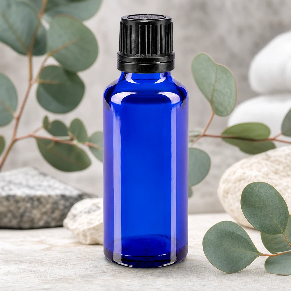 Bottiglia da 30ml blu (Glo.) GR OV nero/8mm ApoGlas Piccola boccetta di vetro blu da 30 ml con tappo di sicurezza nero, davanti a ramoscelli di eucalipto