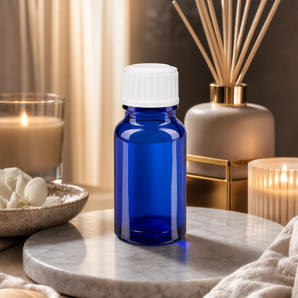 Flacone di vetro blu da 10 ml con tappo bianco su un vassoio di marmo, circondato da candele e un diffusore di profumo per ambienti