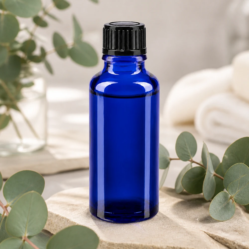 Flacone di vetro da 30 ml blu cobalto con tappo dosatore nero, appoggiato su una pietra naturale con ramoscelli di eucalipto