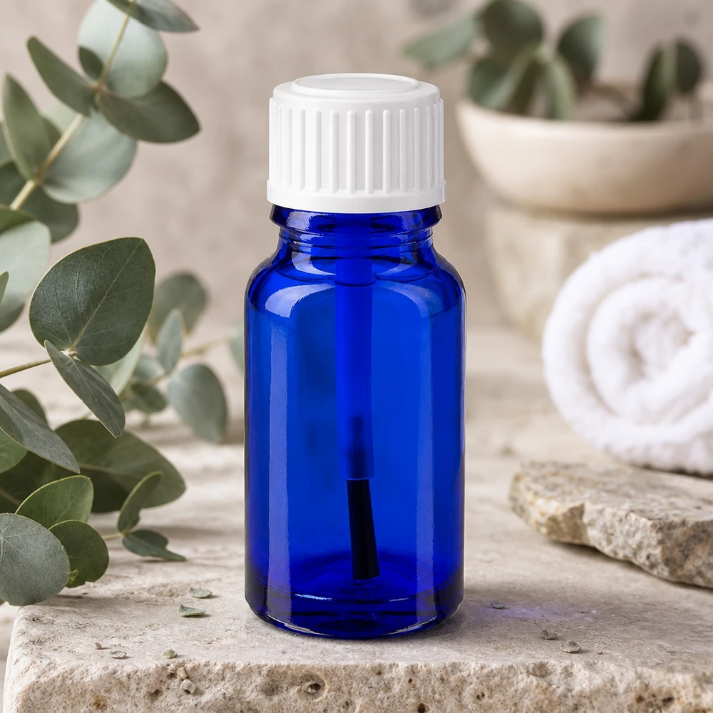 Fioletto di vetro blu da 10 ml con pennellino bianco accanto a ramoscelli di eucalipto su pietra naturale