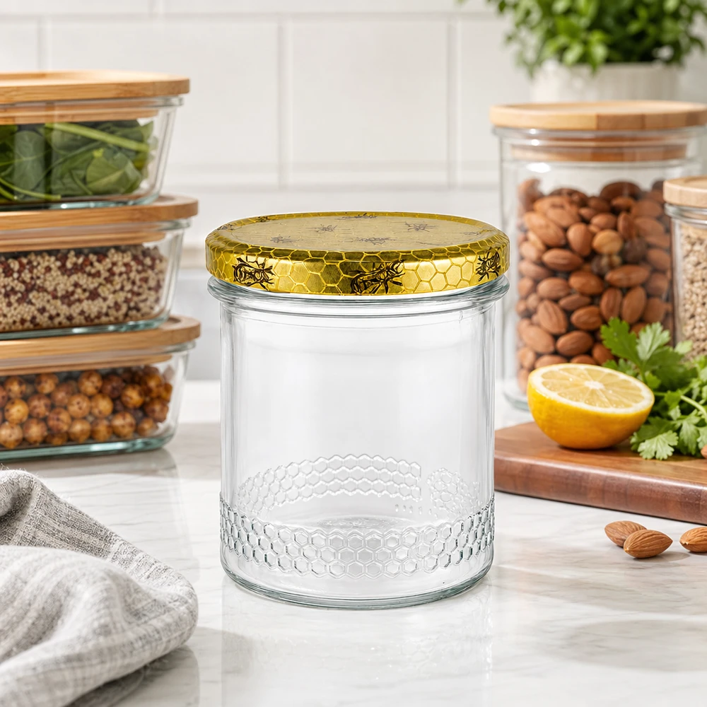 Vasetto per miele da 560 g con capsula a favo BasicSeal UNiTWIST Vasetto di miele da 400 ml con coperchio dorato a nido d'ape sul piano di lavoro della cucina, sullo sfondo vasetti con frutta secca